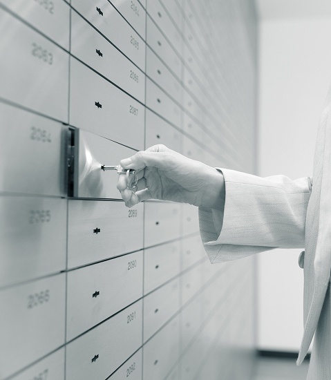 EIne Hand schließt mit einem Schlüssel ein kleines Schließfach in einer Wand voller Schließfächer auf.